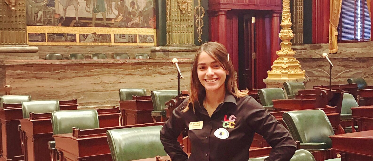 A young woman stands with her hands in her hips in the middle of a large congressional assembly room.