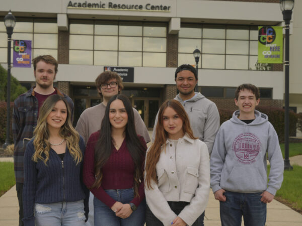 A group of six college students standing together outside the Academic Resource Center on an LCCC campus walkway.