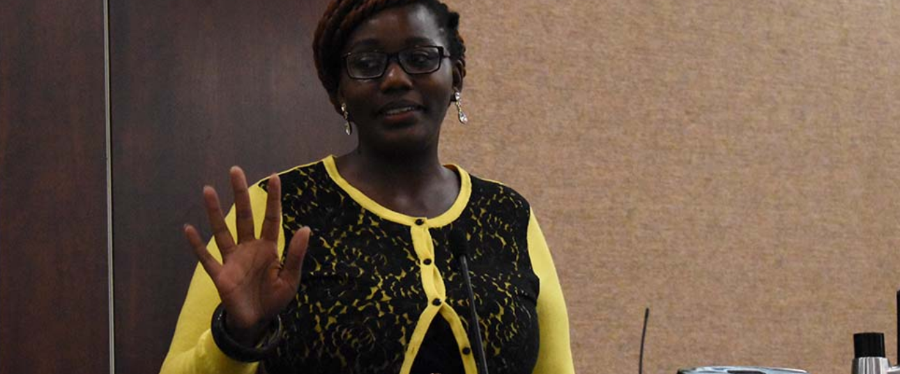 An African American woman in a black and yellow blouse gestures while talking.