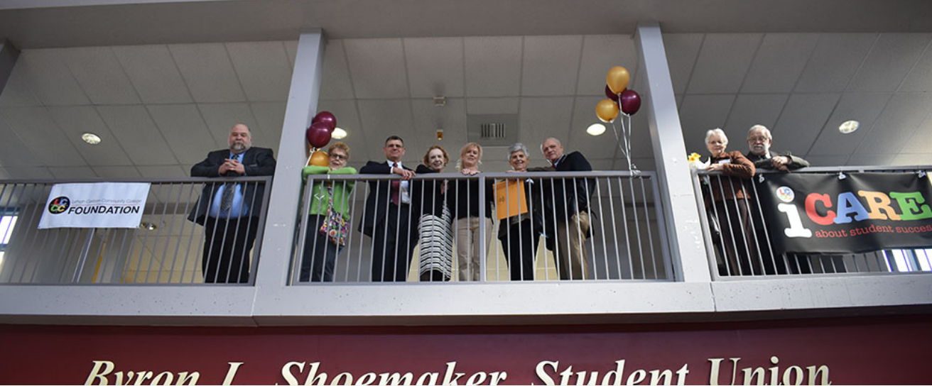 A group of people look down from a balcony they are standing behind.