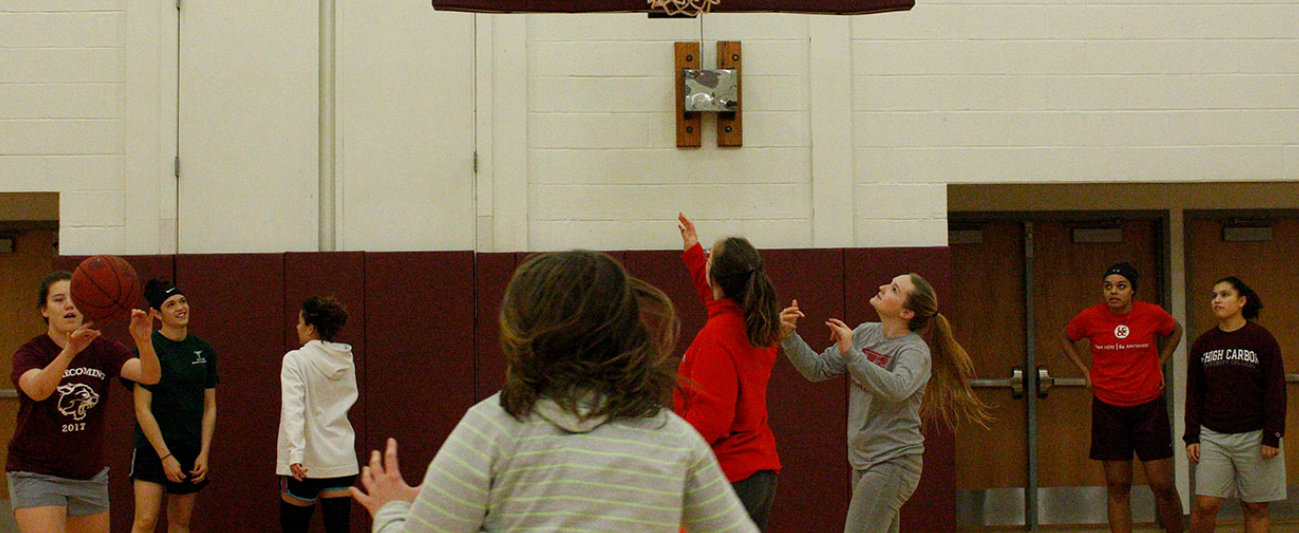 A group of young women dressed in plain clothes play basketball in an indoor court.