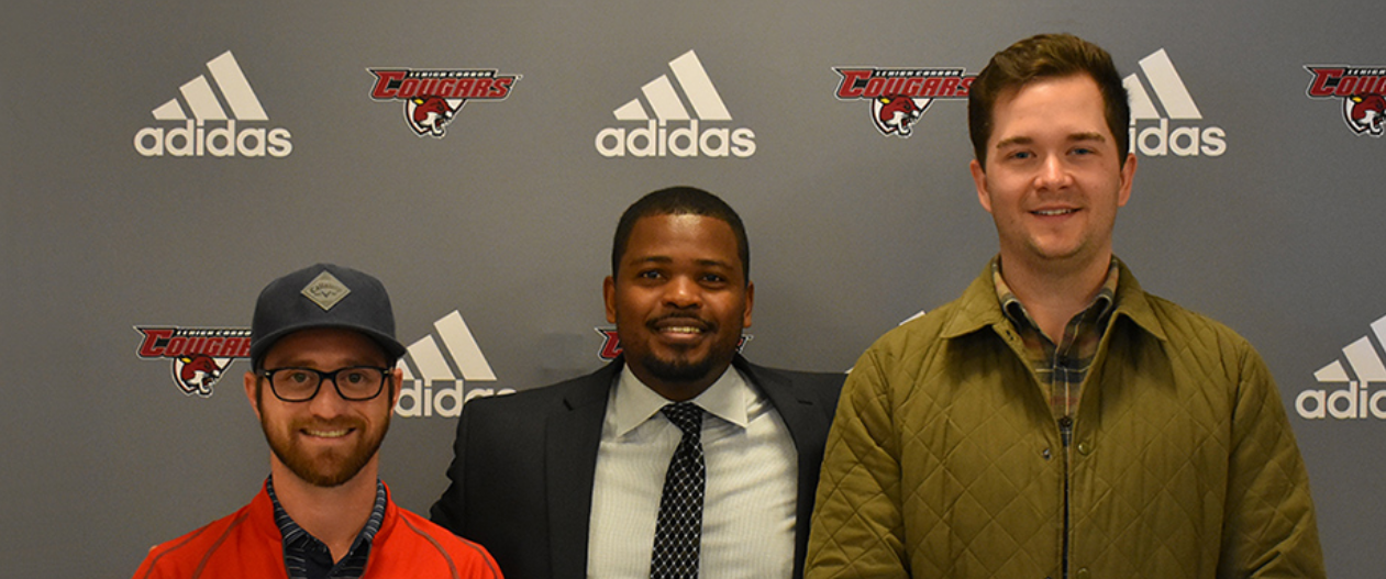 Three men pose for a photo in front of a wall featuring the LCCC Cougarsports logo and the Adidas logo.