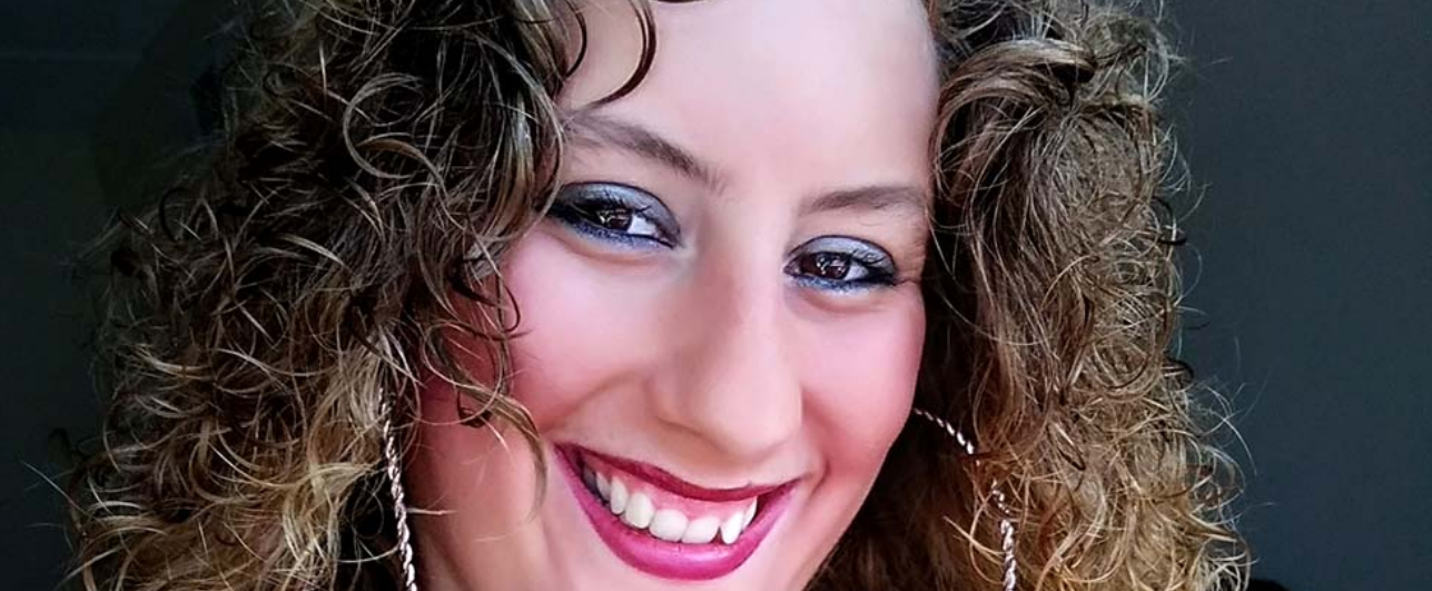 Close up of a woman's face. The woman has curly hair and big silver hoop earrings.