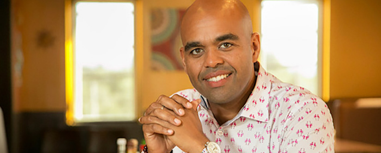 A man in a button down shirt sits with his hands folded.