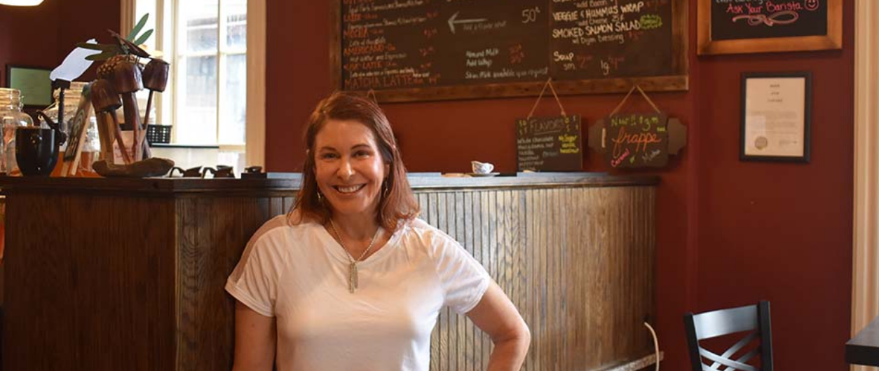 A woman wearing a white t-shirt poses for a photo in front of a coffee bar.