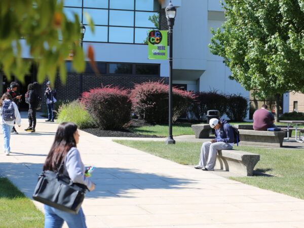Students on a sunny courtyard plaza at Lehigh Carbon Community College (LCCC), with a modern brick building, trees, and an LCCC banner in the background.