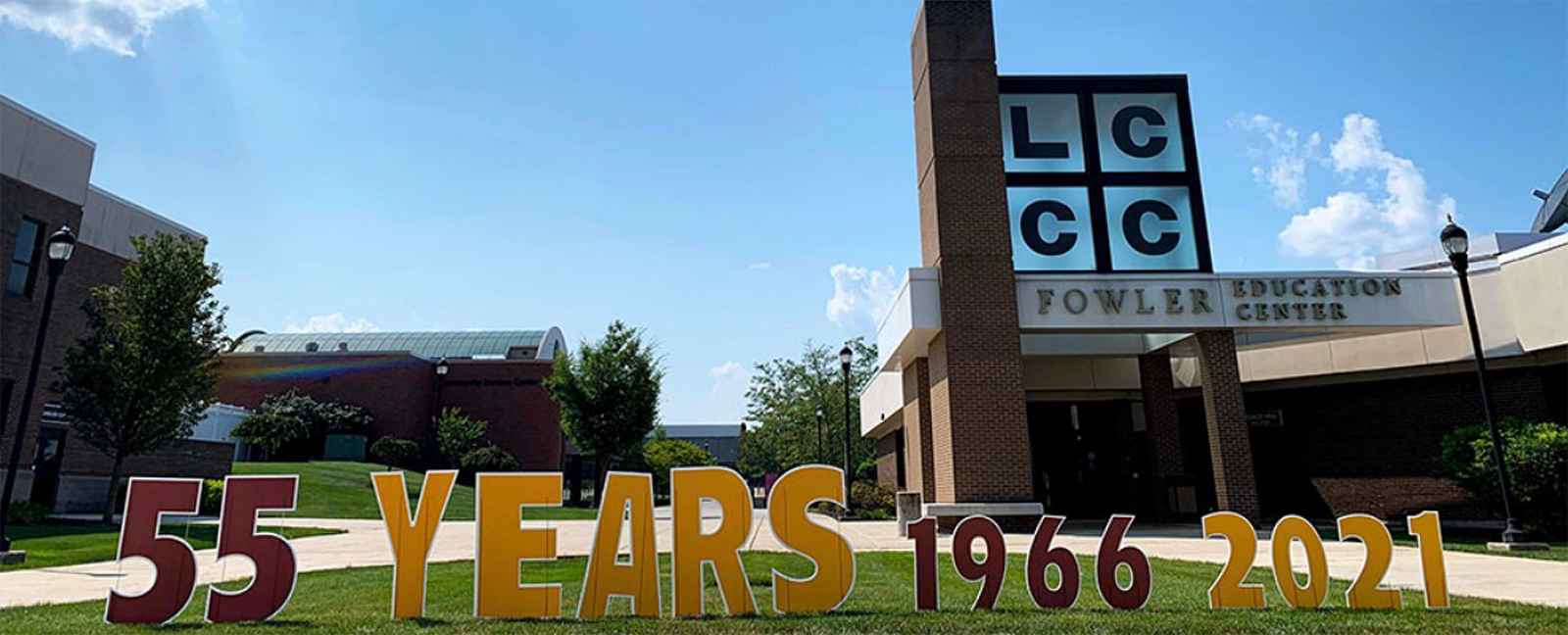 Lawn signs that read "55 Years, 1966, 2021" are in front of a building with windows that say LCCC.
