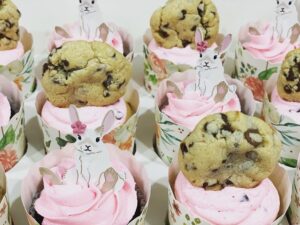 Cupcakes with pink frosting and topped with chocolate chip cookies.