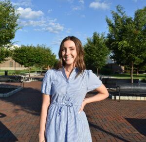 A woman stands with one hand on her hip and smiles at the camera while standing outside the main campus of LCCC.