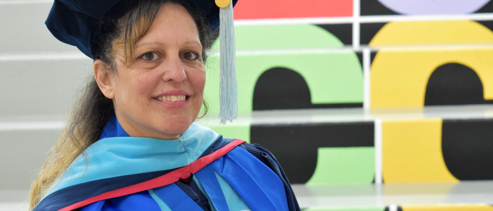 A woman stands in doctoral regalia in front of steps that have the LCCC logo on them.