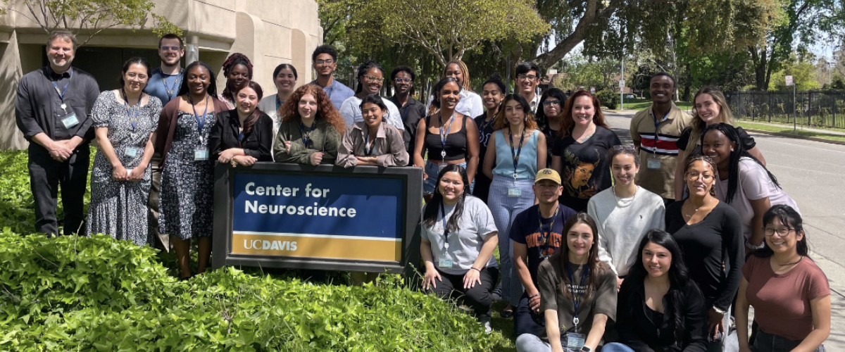A large group of people pose in front of the exterior sign for the Center for Neuroscience at UC Davis.