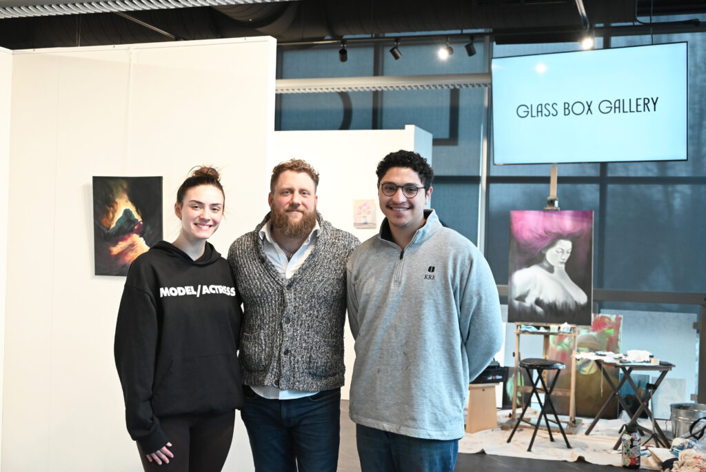 From left to right, Alice Frank, Jeremy Siedt and Alex Ho stand together in the Glass Box Gallery with art on display in the background.