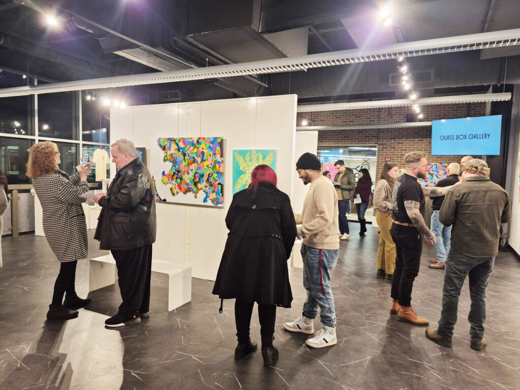 Exhibit reception attendees stand and mingle amongst the art in the Glass Box Gallery.