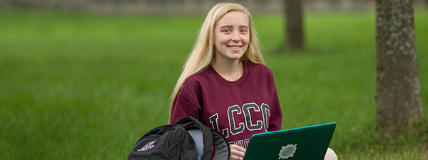 Student outside in grass with laptop