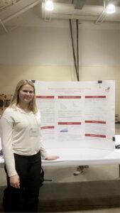 A woman in a white sweater stands next to a poster board presentation.