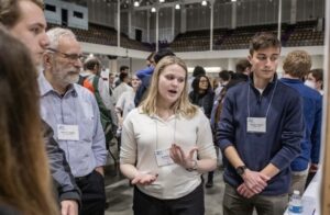 A woman gestures while talking in the middle of a conference expo floor.