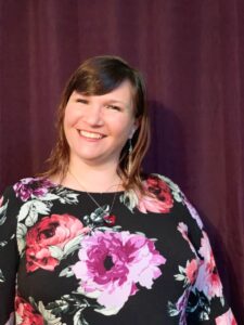 Jenny Pacanowski smiles in front of a maroon background