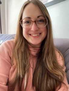 A woman in a pink shirt and glasses smiles at the camera.