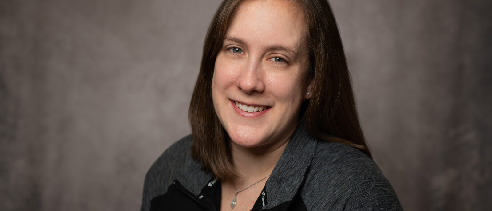 A young woman in an Eagles pullover smiles for the camera on a photography backdrop.