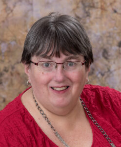 Professional portrait of a woman with short hair and glasses wearing a red blouse.