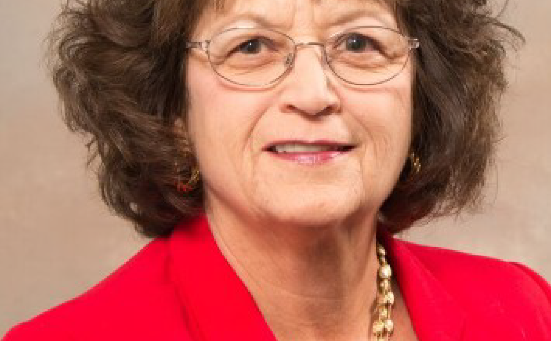 Portrait photo of Nancy Dischinat - a woman with brown shoulder length hair and glasses wearing a red suit jacket.