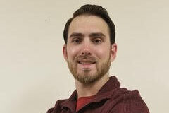 Professional portrait of a man with brown hair and cropped beard with arms crossed.