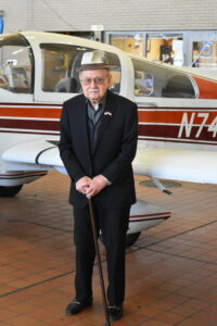 A man in a hat and holding a cane stands in front of a small plane.
