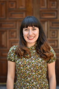 Dr. Vanessa Ringle smiles directly into the camera while wearing a green floral blouse and stands in front of a wooden door.