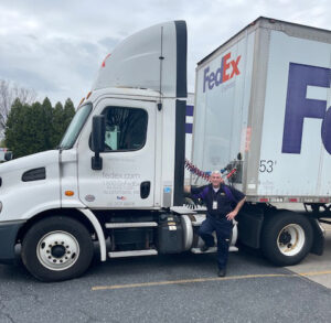A man stands next to the cab of a FedEx truck.