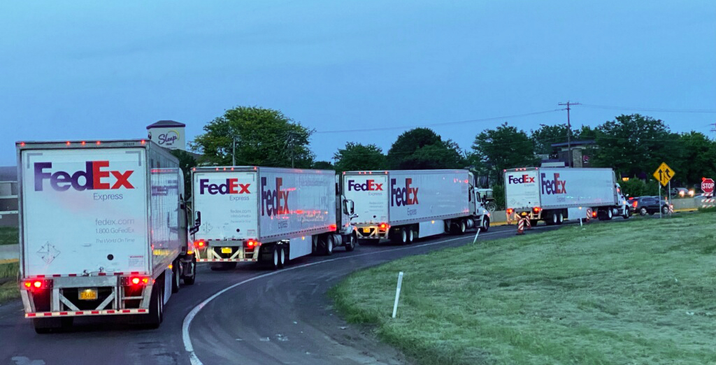 A line of FedEx trucks line up on an on ramp.