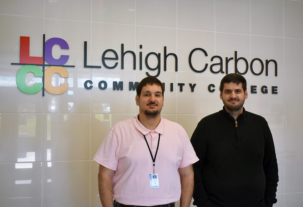 Two men stand side by side in front of a wall featuring the Lehigh Carbon Community College logo.