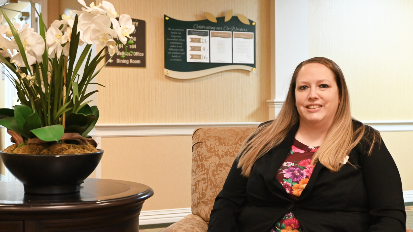 Vanessa Berger sits in the lobby of Country Meadows Senior Living, next to a table holding a pot of fake flowers.