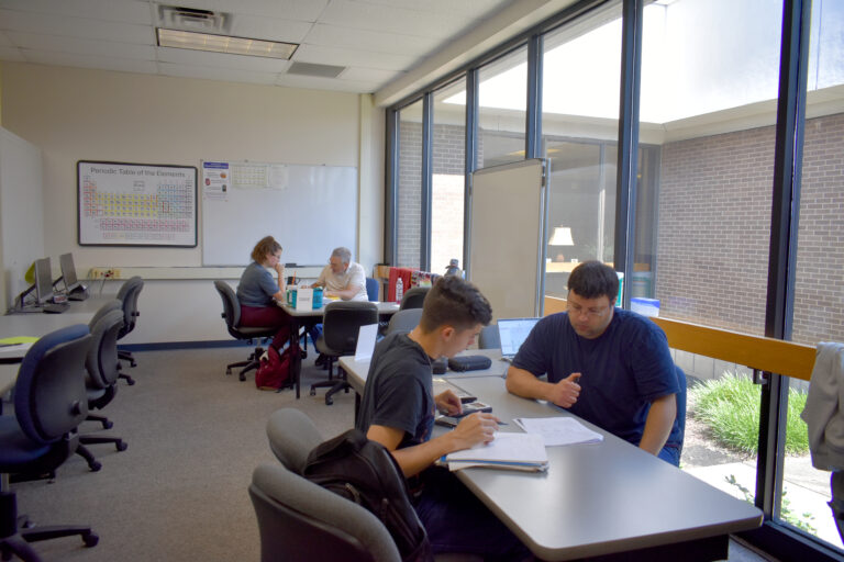 Image shows two tutors sitting and working with two students in the Tutoring Center.