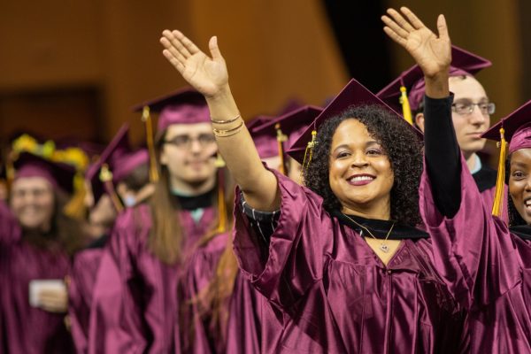 Students in caps and gowns waving at graduation